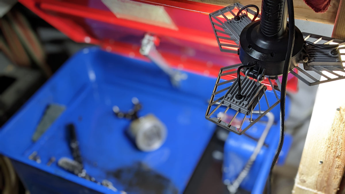 Overhead shot of the TRiLIGHT ShopLight V2 hanging above a solvent tank parts washer with a V8 piston and connecting rod in the basin, lighting the work area.