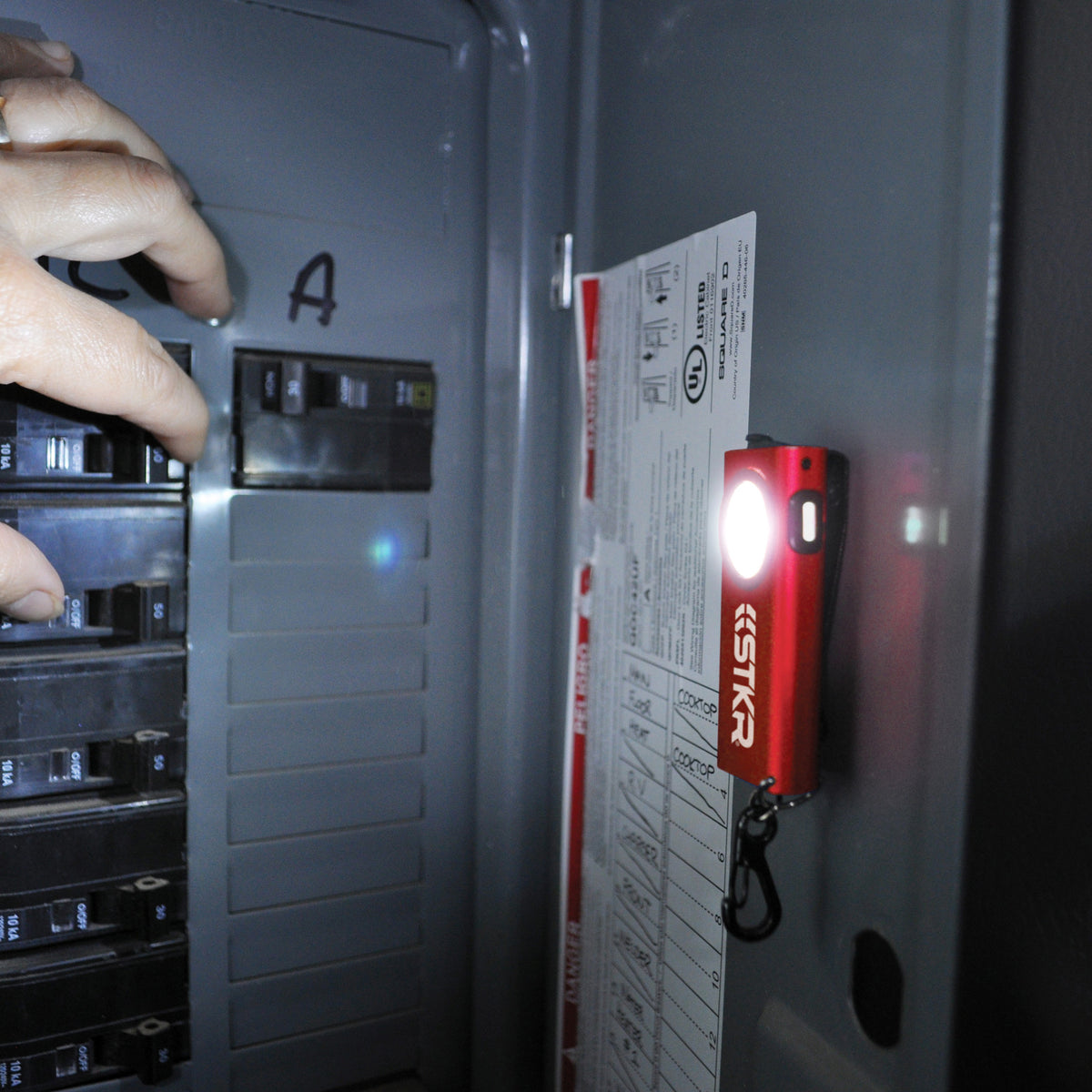 SlimJIMMY magnetically attached to the inside door of a breaker panel lighting it up for a hand that's switching a breaker