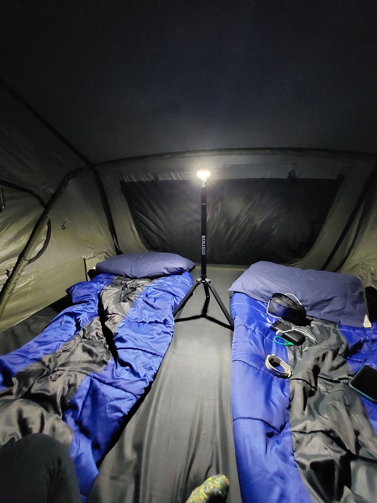 Camping setup inside a tent with blue sleeping bags and a tripod-mounted lit up by a FLi-LITE.